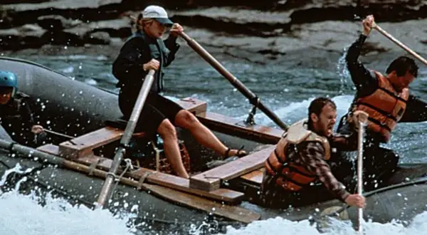 Il cast di The River Wild affronta rapide impetuose su un gommone, remando con forza per sopravvivere.