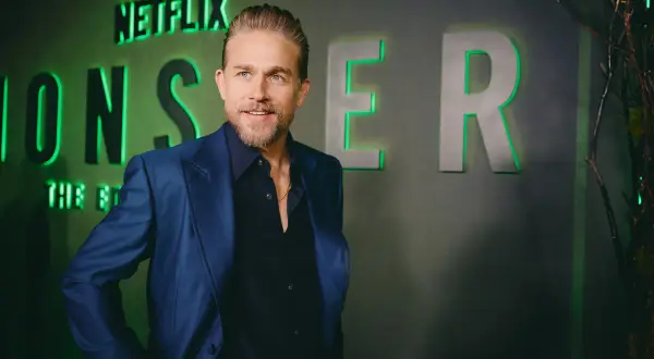 Charlie Hunnam, protagonista di film e programmi TV, posa con un sorriso davanti al logo Netflix.