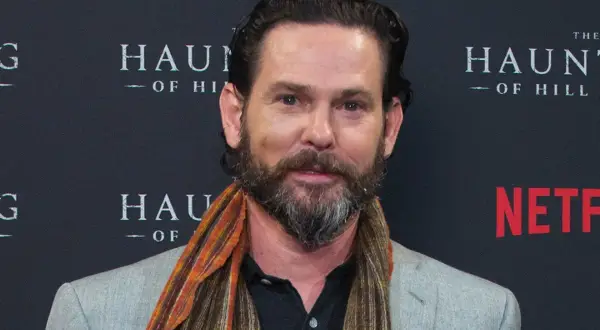 Henry Thomas, noto per i suoi film e programmi TV, sorride con una sciarpa colorata.