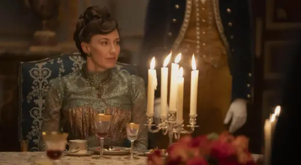 Una donna elegante, in abito d'epoca, siede a tavola durante un sontuoso banchetto, un'immagine che evoca lo sfarzo e le tensioni sociali della Gilded Age.