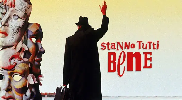 Un uomo con cappello e valigia saluta, circondato da maschere colorate. Il titolo del film "Stanno tutti bene" campeggia in rosso.