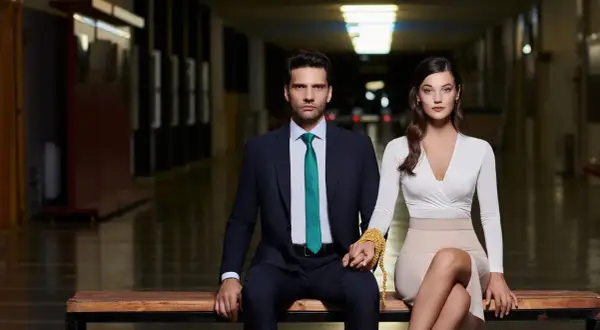 Coppia elegante seduta su una panca, lui in abito scuro, lei in abito bianco. Le loro mani sono unite da una catena dorata, simbolo dei loro segreti di famiglia.