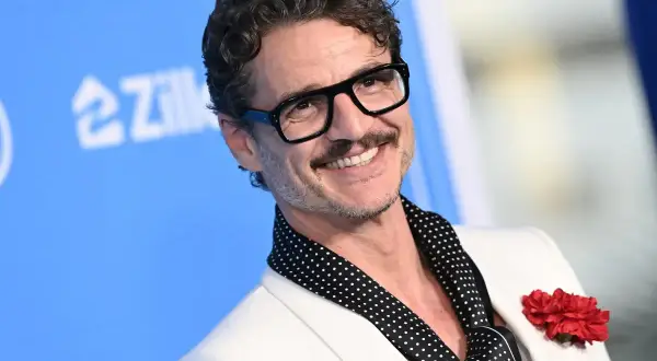 Pedro Pascal sorride con occhiali neri e un fiore rosso sul bavero. La sua vita privata è un mistero affascinante.