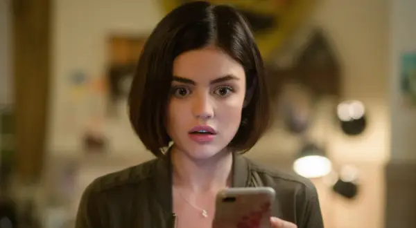 Lucy Hale, protagonista di film e programmi TV, guarda sorpresa il suo telefono.