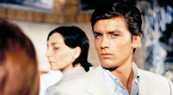 Alain Delon, icona di stile, in una scena che evoca i suoi film più belli. Sguardo intenso, fascino intramontabile.