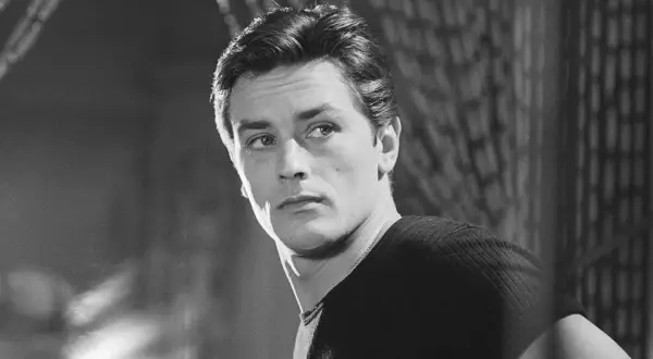 Alain Delon da ragazzo, con sguardo intenso e capelli pettinati all'indietro, indossa una maglia a coste.
