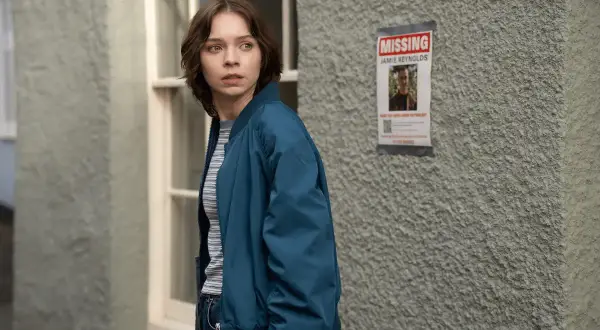 Ragazza preoccupata guarda un volantino "MISSING JAMIE REYNOLDS". La serie tv "come uccidono le brave ragazze" esplora misteri oscuri.