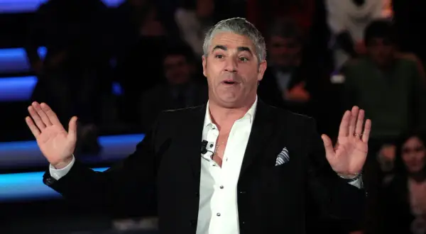 Izzo, attore comico, con le mani aperte sul palco, pronto a far ridere il pubblico.
