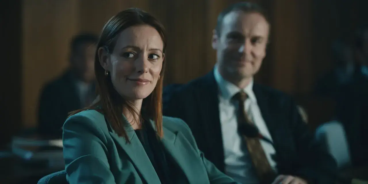 Donna con tailleur verde acqua sorride, mentre un uomo in giacca e cravatta la osserva. Forse stanno discutendo del codice da un miliardo di dollari.