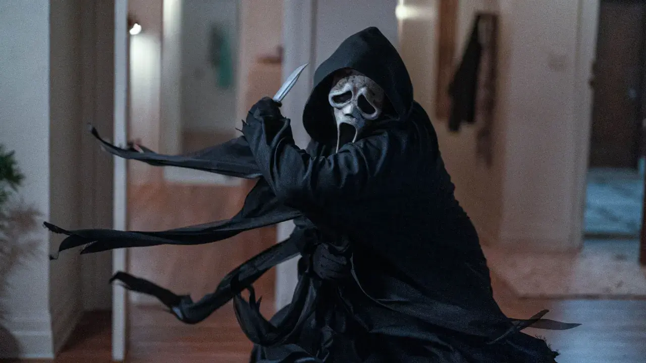 Ghostface, icona del film di Scream, brandisce un coltello con la sua maschera spettrale e il mantello svolazzante.