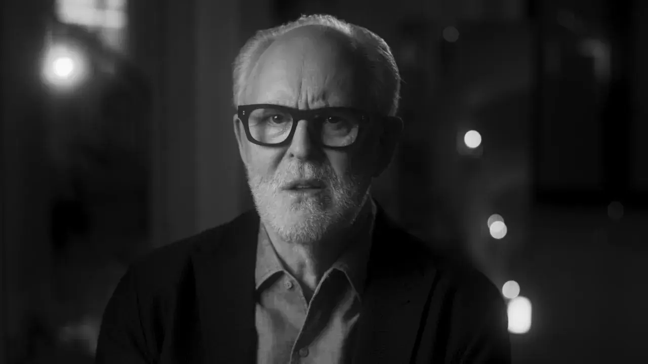 Primo piano in bianco e nero di John Lithgow con occhiali, che riflette sulla sua carriera nei film e programmi TV.