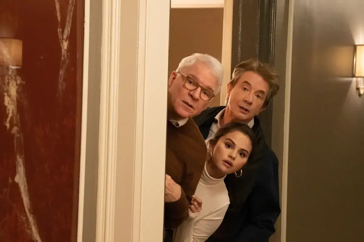 I tre protagonisti di "Only Murders in the Building" sbirciano curiosi da dietro una porta, pronti a svelare un nuovo mistero.