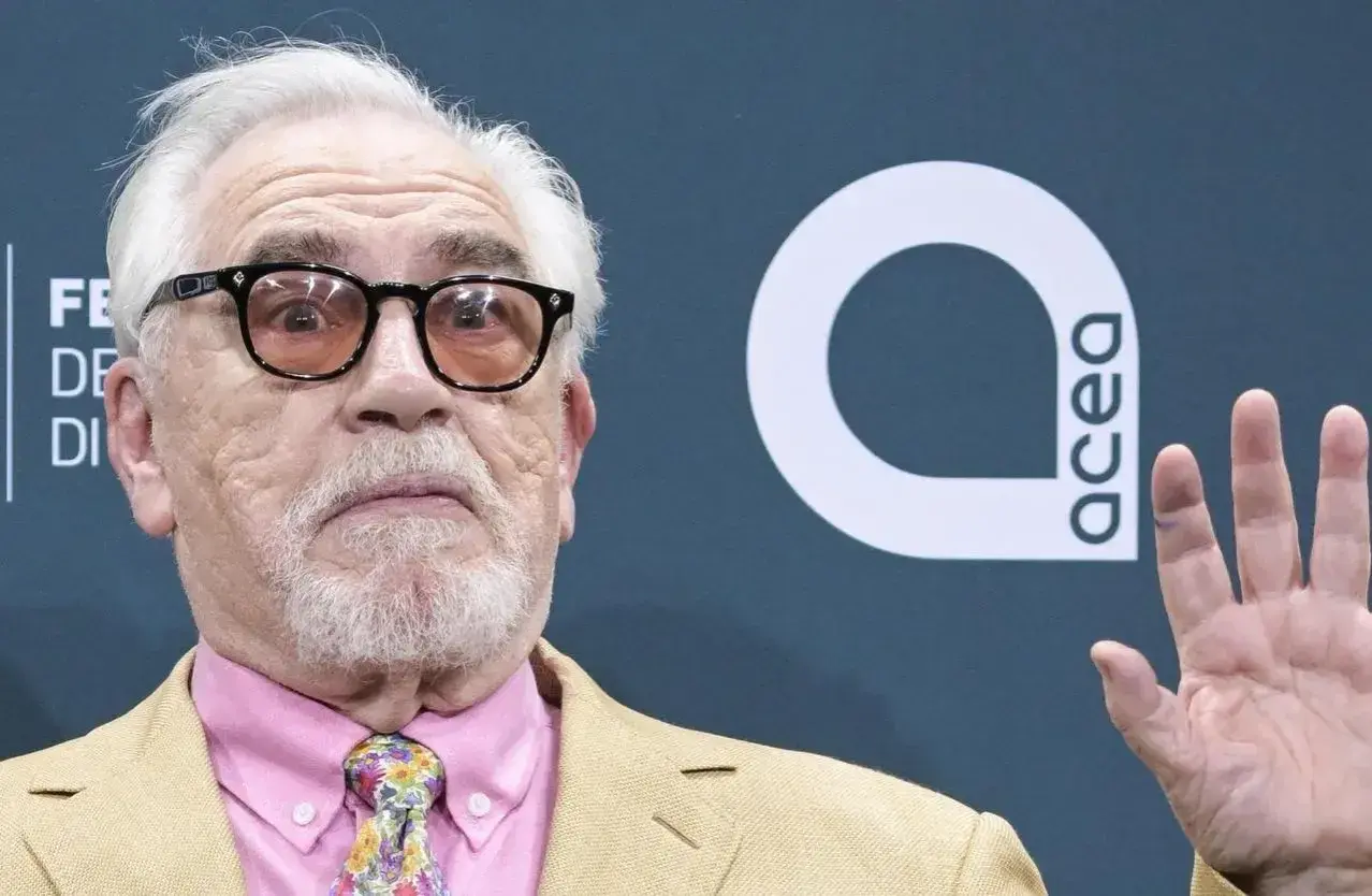 Brian Cox, noto per i suoi film e programmi TV, con occhiali e cravatta colorata.