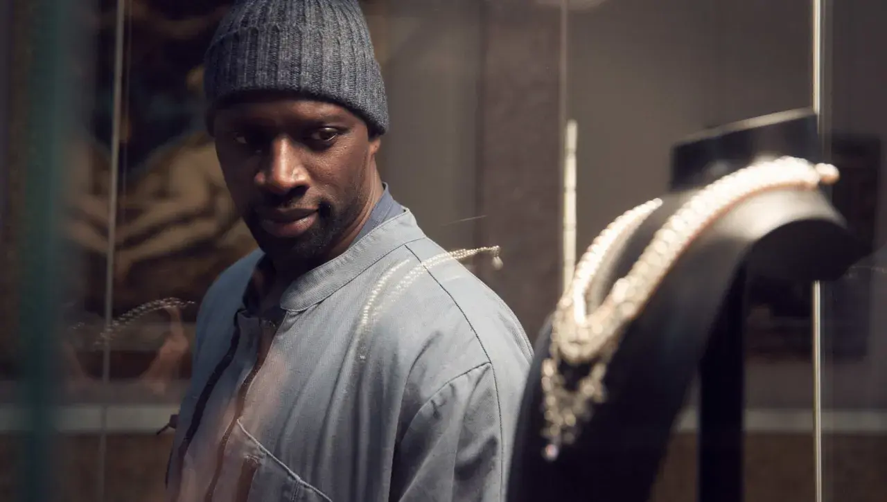 Omar Sy, protagonista di film e programmi TV, osserva con astuzia una collana di perle in una vetrina.