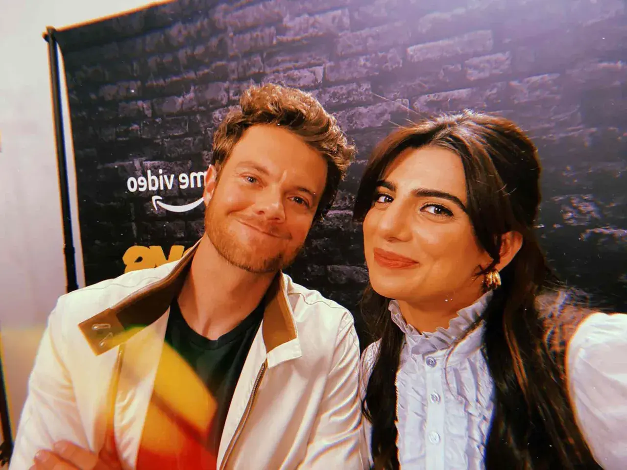 Jack Quaid sorride con la sua fidanzata, una foto scattata davanti a uno sfondo con il logo di Amazon.