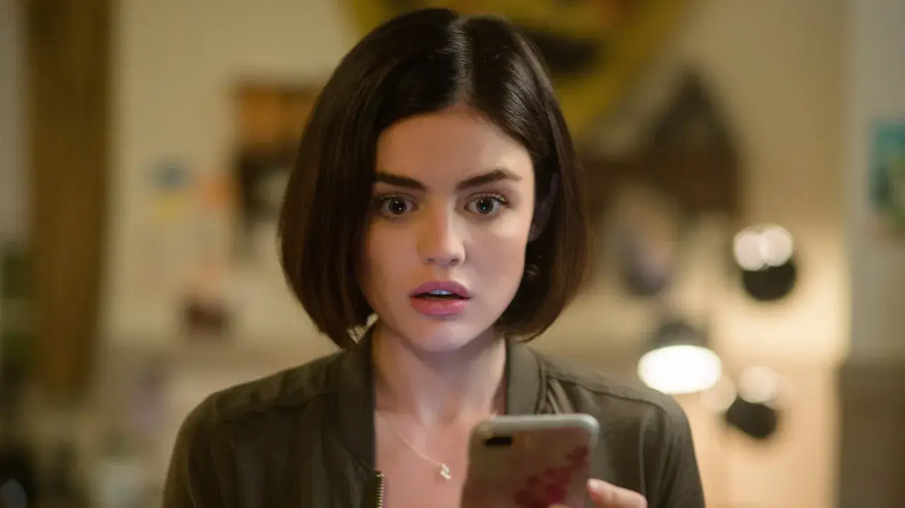 Lucy Hale, protagonista di film e programmi TV, guarda sorpresa il suo telefono.