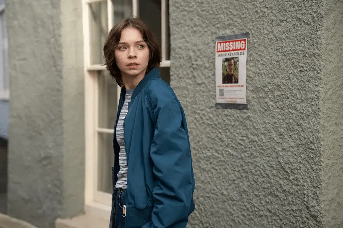 Ragazza preoccupata guarda un volantino "MISSING JAMIE REYNOLDS". La serie tv "come uccidono le brave ragazze" esplora misteri oscuri.