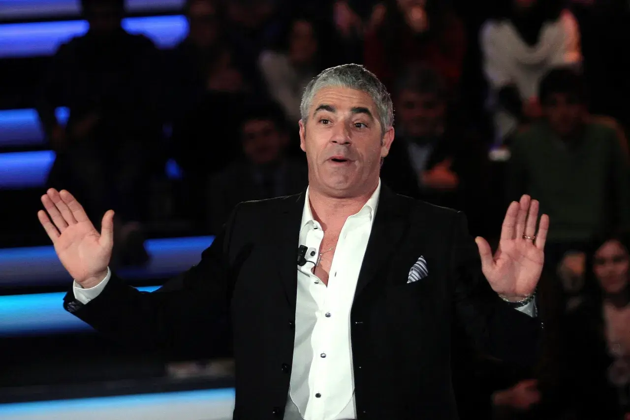 Izzo, attore comico, con le mani aperte sul palco, pronto a far ridere il pubblico.