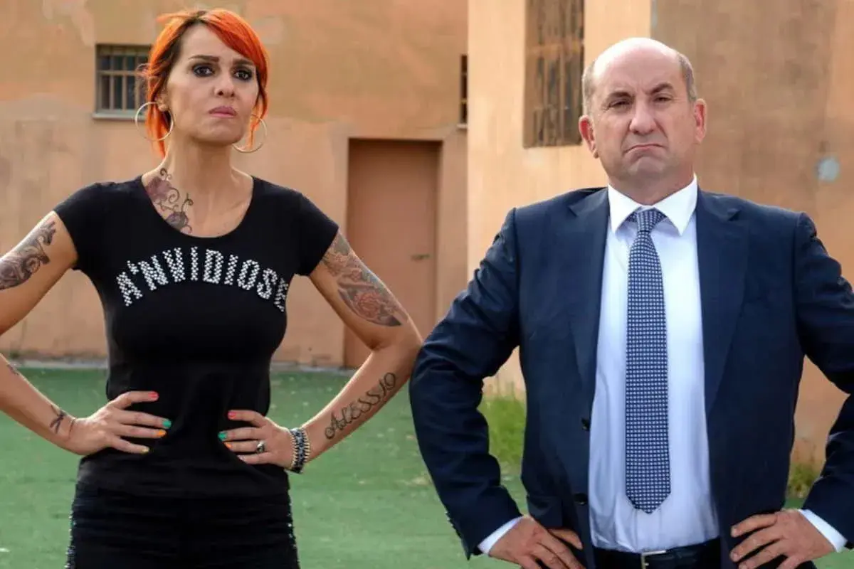 Donna tatuata con maglietta "A'n'vidiosə" e uomo in giacca e cravatta, con espressioni serie, come un gatto in tangenziale 2.