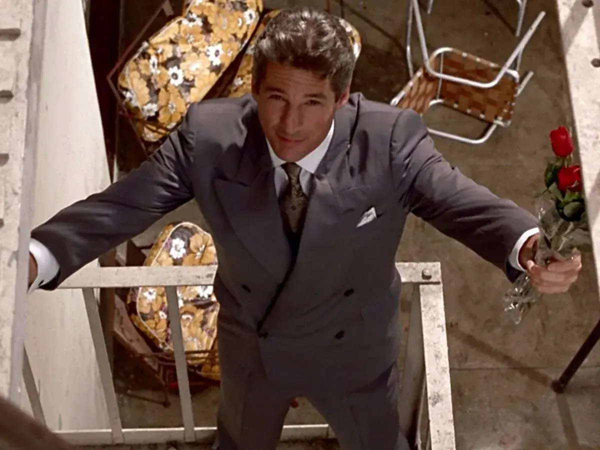 Richard Gere, iconico in "American Gigolo film", con un mazzo di rose rosse, elegante in abito grigio.