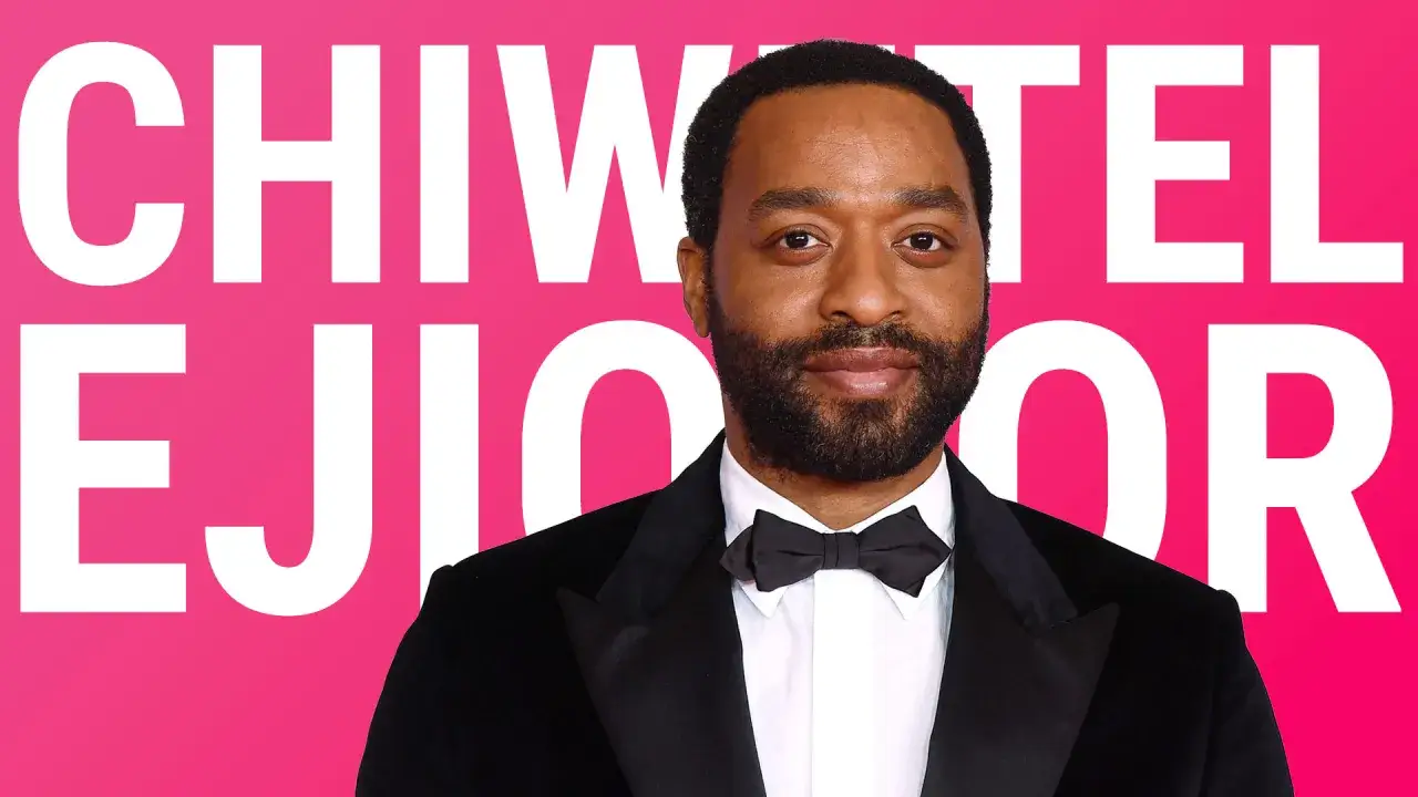 Chiwetel Ejiofor, protagonista di film acclamati, indossa un elegante smoking su sfondo rosa acceso con il suo nome in grandi lettere bianche.