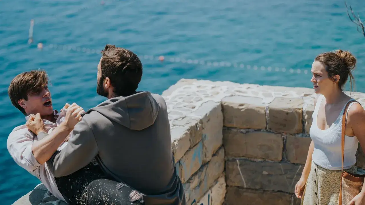 Un weekend away finito male: due uomini litigano su una scogliera, una donna li osserva preoccupata.
