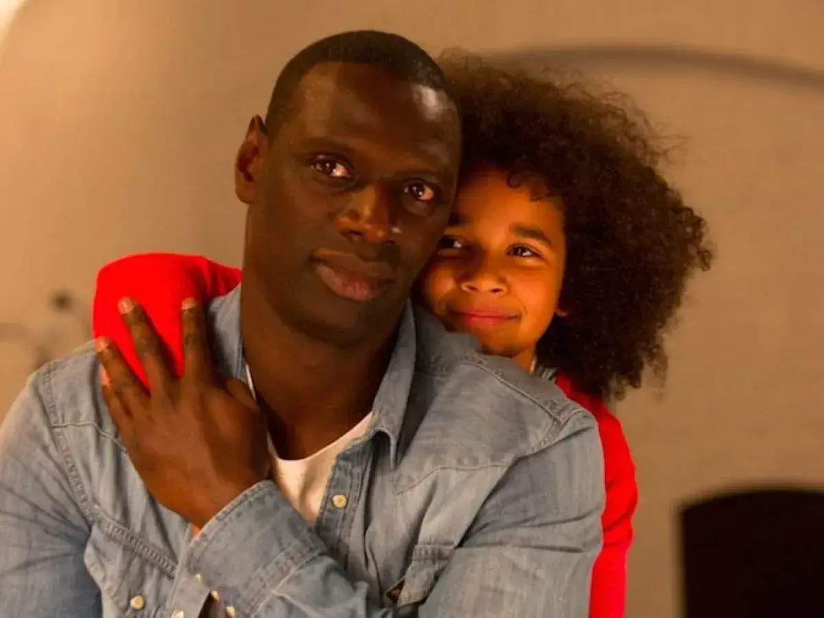 Omar Sy abbraccia affettuosamente una bambina. Un momento tenero che ricorda i suoi film e programmi TV.