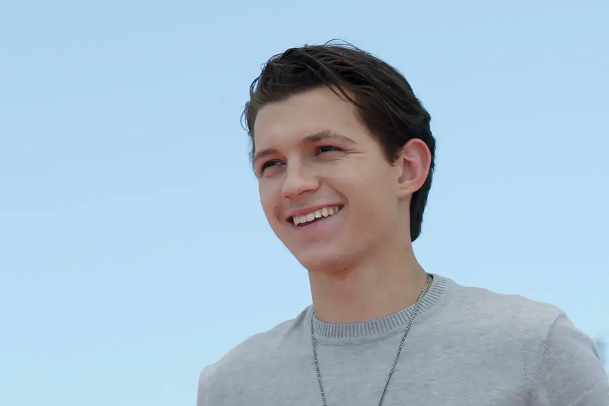 Tom Holland sorride con un maglione grigio. Chissà quanti anni ha Tom Holland?