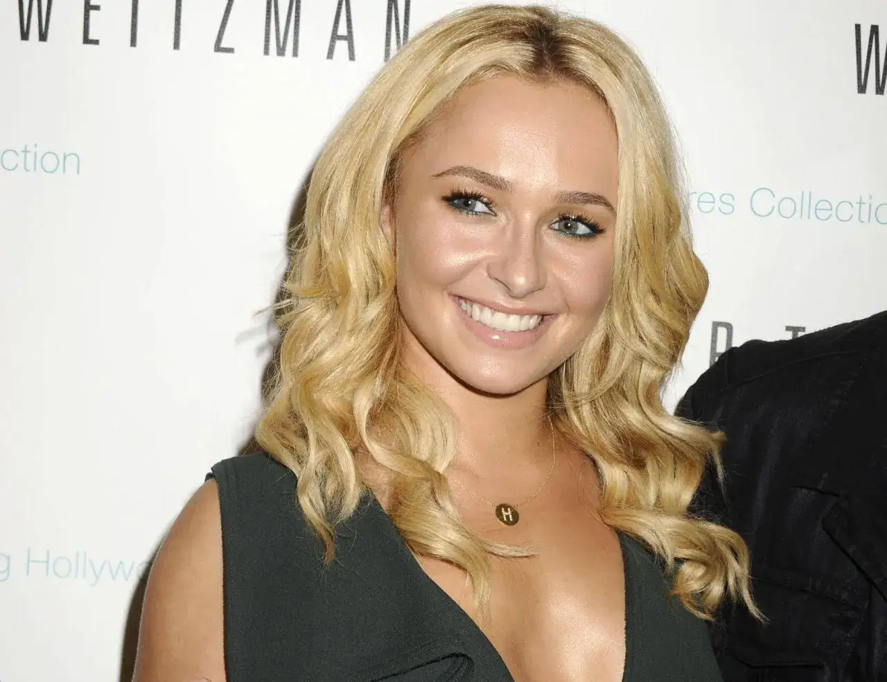 Hayden Panettiere oggi, con capelli biondi mossi e un sorriso radioso, indossa una collana con la lettera H.