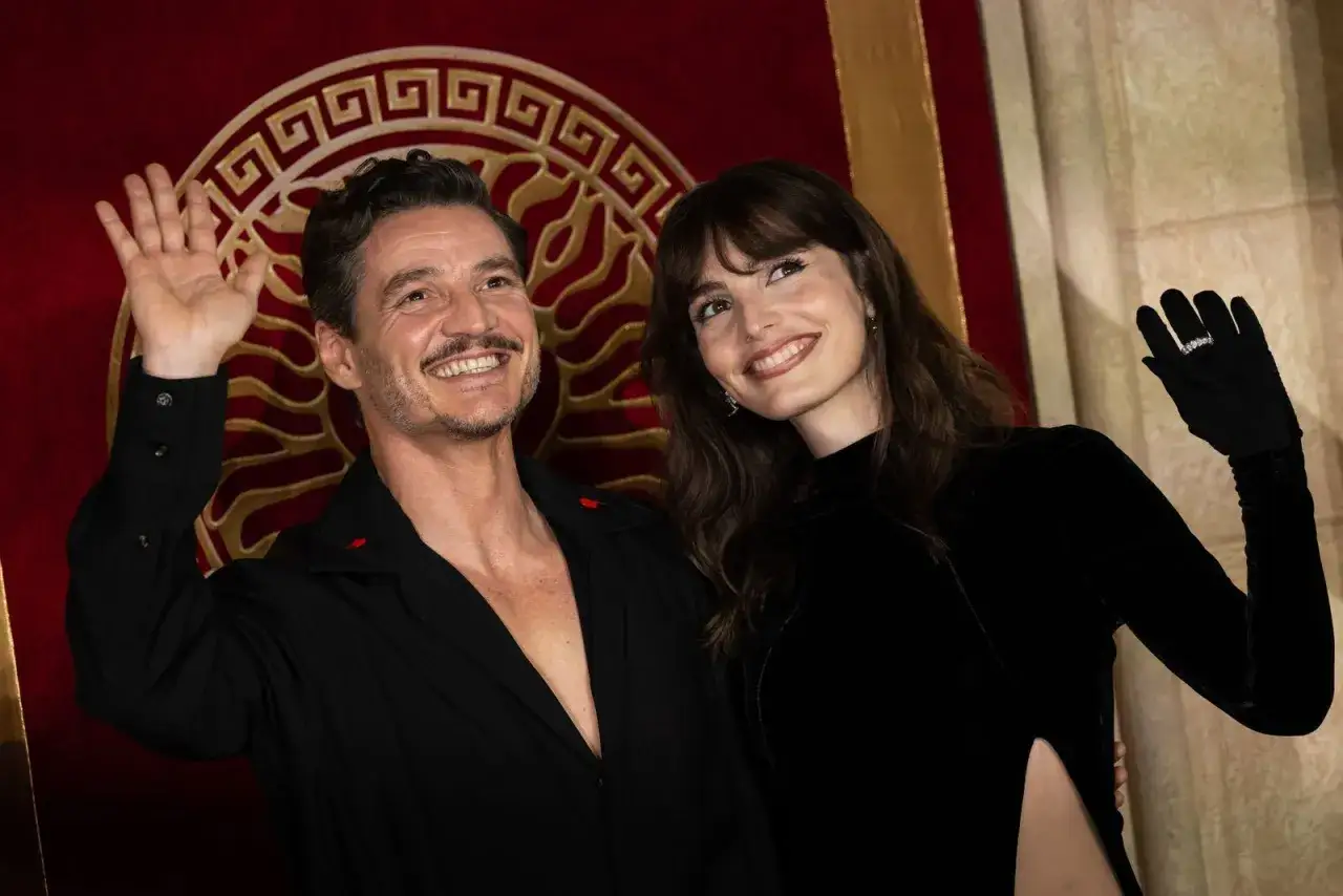 Pedro Pascal sorride e saluta, accanto a una donna con un abito nero. Un'immagine che cattura un momento della sua vita privata.
