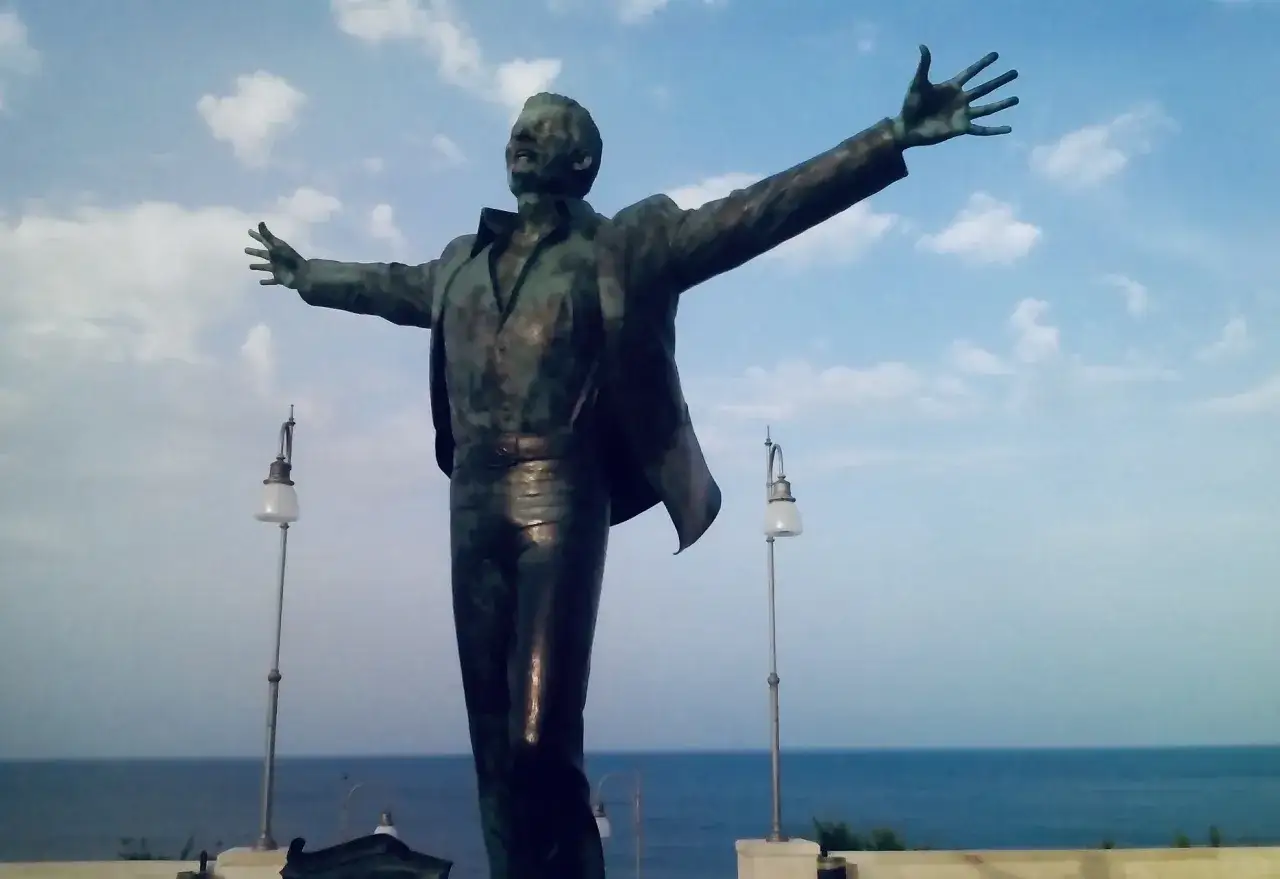 Statua di Domenico Modugno, simbolo della sua nascita artistica, con le braccia aperte verso il mare e il cielo azzurro.