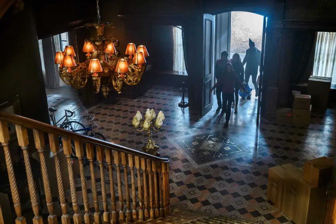 Un gruppo di persone entra in una casa misteriosa, forse alla ricerca di segreti e chiavi magiche, sotto un lampadario imponente.