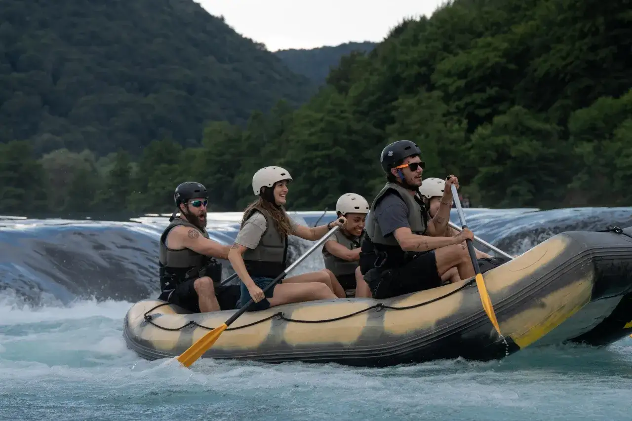 Il cast di The River Wild affronta rapide impetuose su un gommone, con montagne boscose sullo sfondo.
