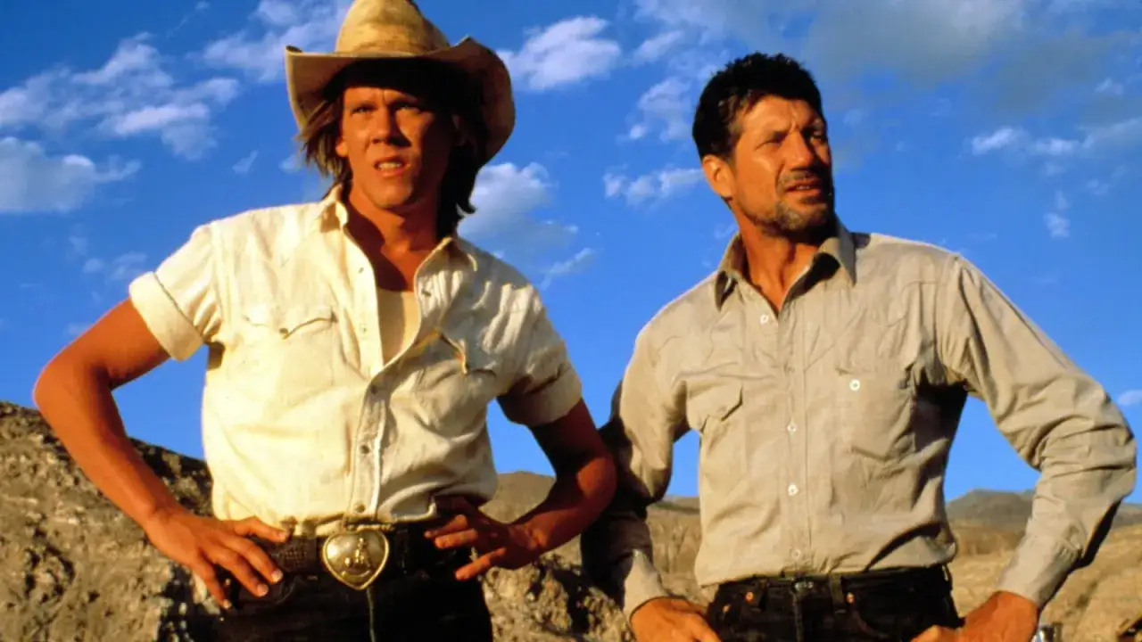 Il cast di Tremors, Kevin Bacon e Fred Ward, in un paesaggio desertico sotto un cielo azzurro.