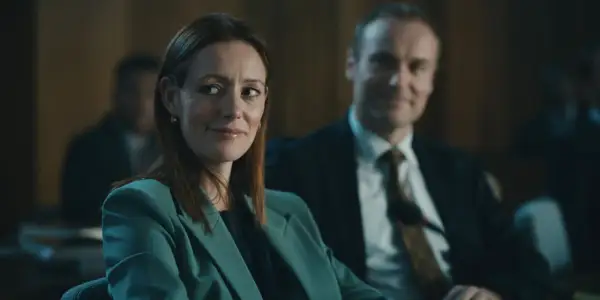 Donna con tailleur verde acqua sorride, mentre un uomo in giacca e cravatta la osserva. Forse stanno discutendo del codice da un miliardo di dollari.