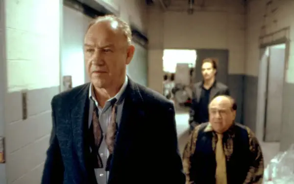 Gene Hackman in un film, cammina con altri due uomini in un corridoio.