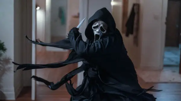Ghostface, icona del film di Scream, brandisce un coltello con la sua maschera spettrale e il mantello svolazzante.