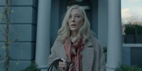 Donna bionda con foulard rosso e cappotto beige, espressione preoccupata. Un'immagine che anticipa un disclaimer serie tv.