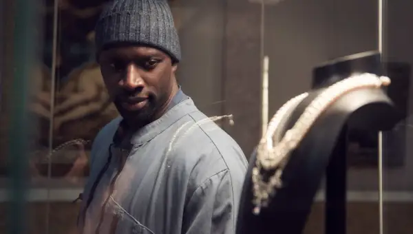 Omar Sy, protagonista di film e programmi TV, osserva con astuzia una collana di perle in una vetrina.