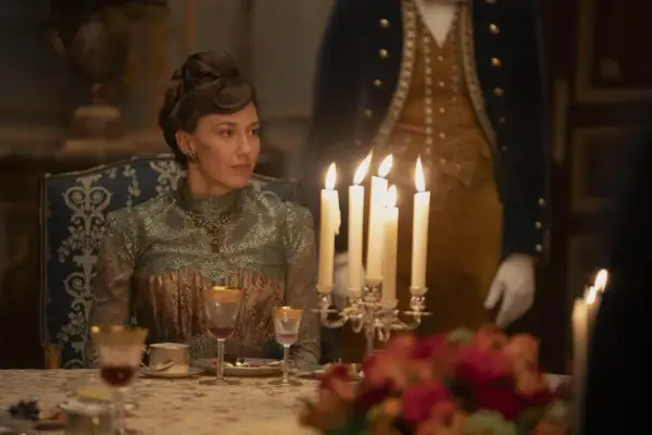 Una donna elegante, in abito d'epoca, siede a tavola durante un sontuoso banchetto, un'immagine che evoca lo sfarzo e le tensioni sociali della Gilded Age.