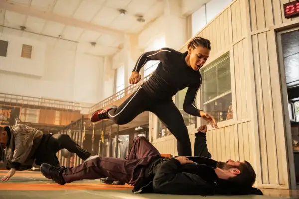 Scena di combattimento intensa, una donna in tuta nera salta su un uomo a terra. Un altro uomo è a terra in background. Un film di 60 minuti pieno d'azione.