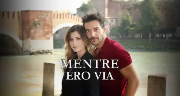 Coppia abbracciata con un ponte sullo sfondo. Il titolo "Mentre ero via" suggerisce una storia di assenza e ritorno.