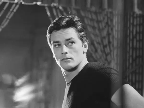 Alain Delon da ragazzo, con sguardo intenso e capelli pettinati all'indietro, indossa una maglia a coste.