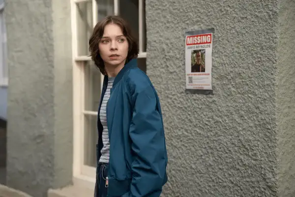 Ragazza preoccupata guarda un volantino "MISSING JAMIE REYNOLDS". La serie tv "come uccidono le brave ragazze" esplora misteri oscuri.